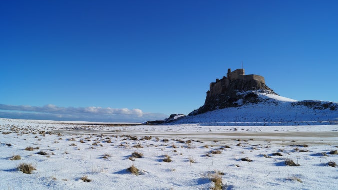 A picture showing Lindisfarne Castle on Holy Island, Northumberland following snowfall in the winter of 2021, with blue sky.